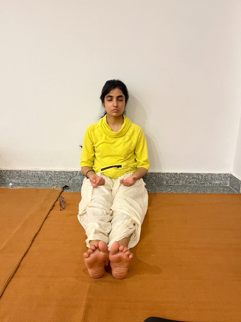 Young woman in seated yoga posture focusing inward on ochre practice mat