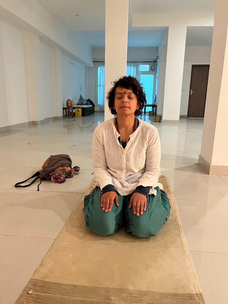 Practitioner in white kurta and green salwar meditating in Vajrasana on natural mat